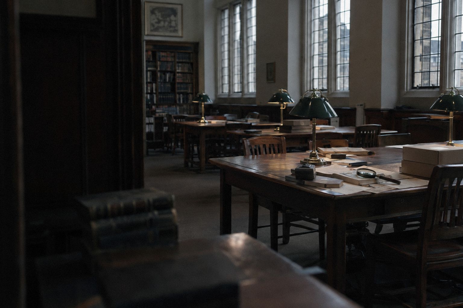 A reading room with green desk lamps and papers on a long table.