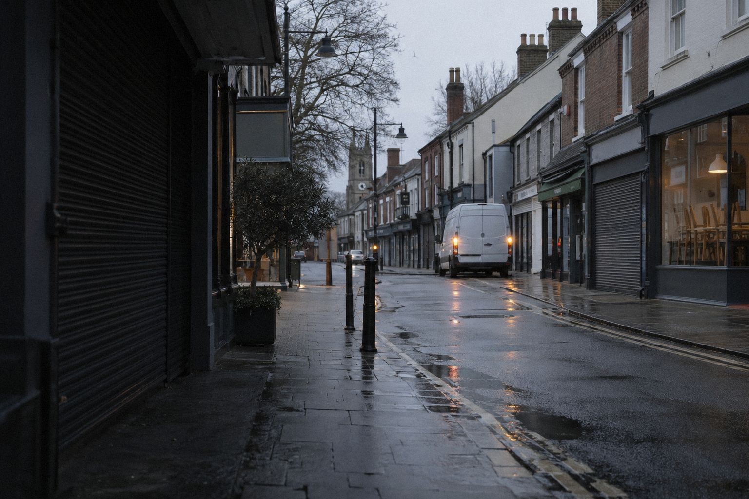 A high street at first light, shops still shuttered and a delivery van parked.