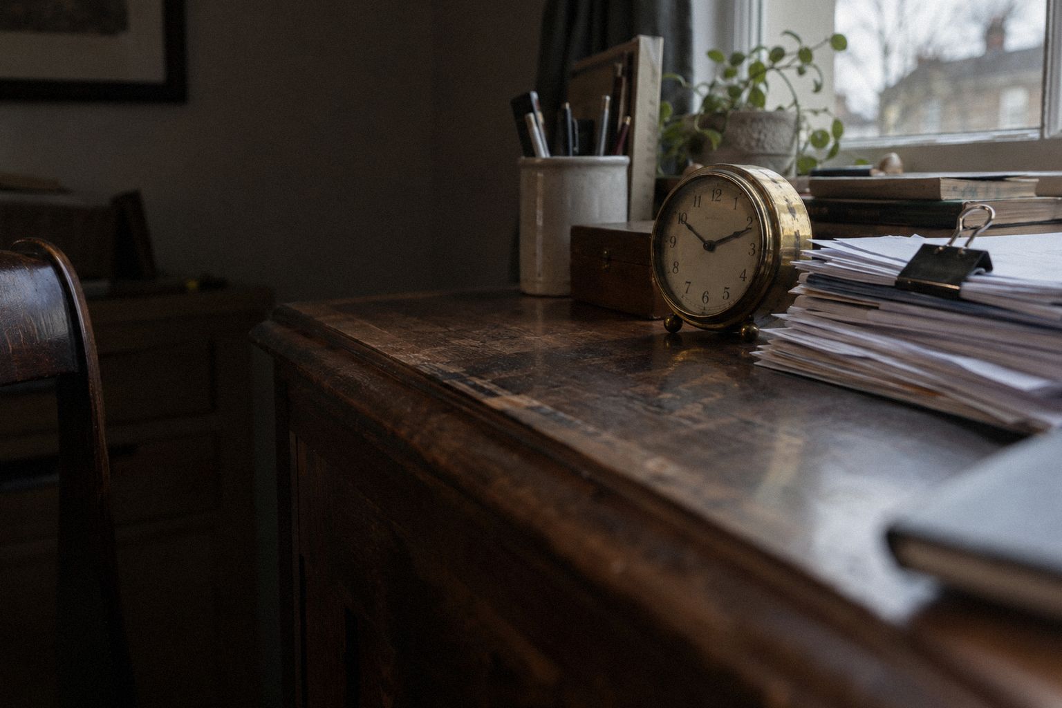 A brass desk clock beside a clipped stack of invoices in low winter light.