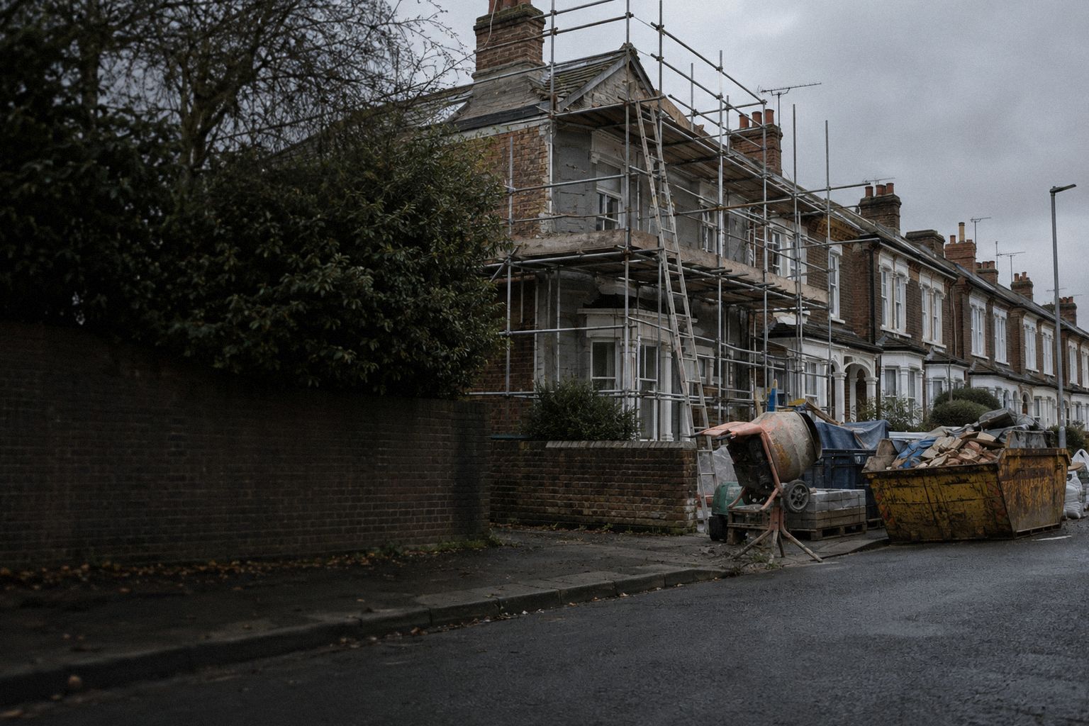 Scaffolding around a terraced house, a cement mixer and a skip outside.