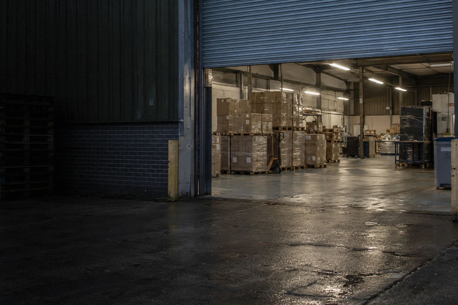 A print works at 6am, the shutter half up and pallets of cartons inside.