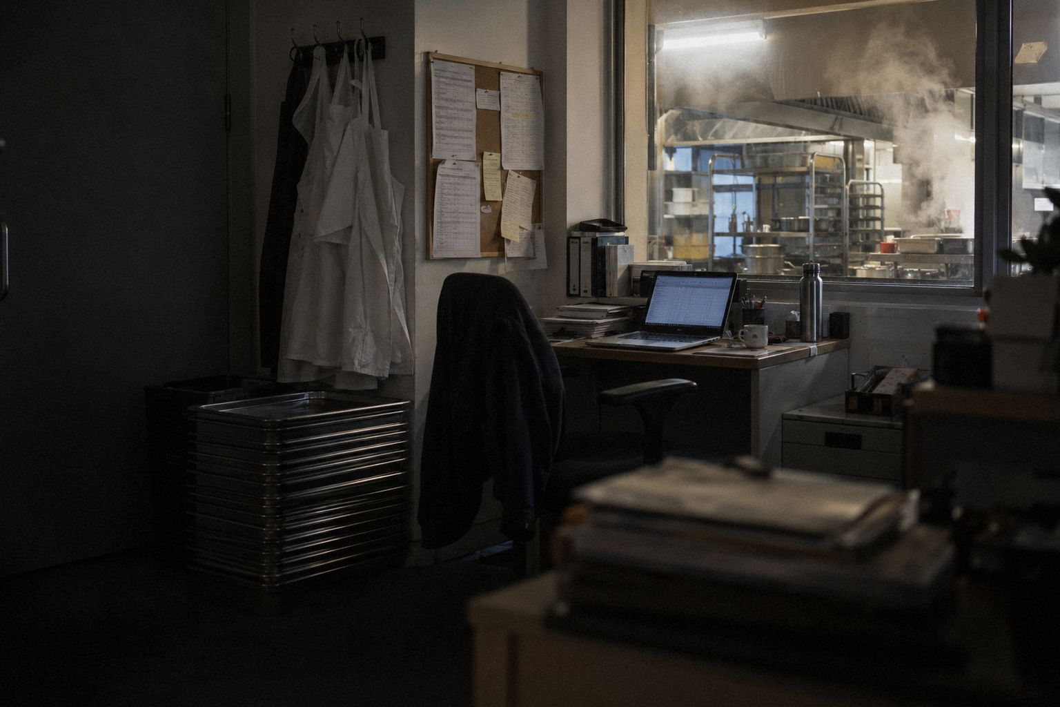 A catering firm's office above the kitchen at 9pm, aprons on a hook.
