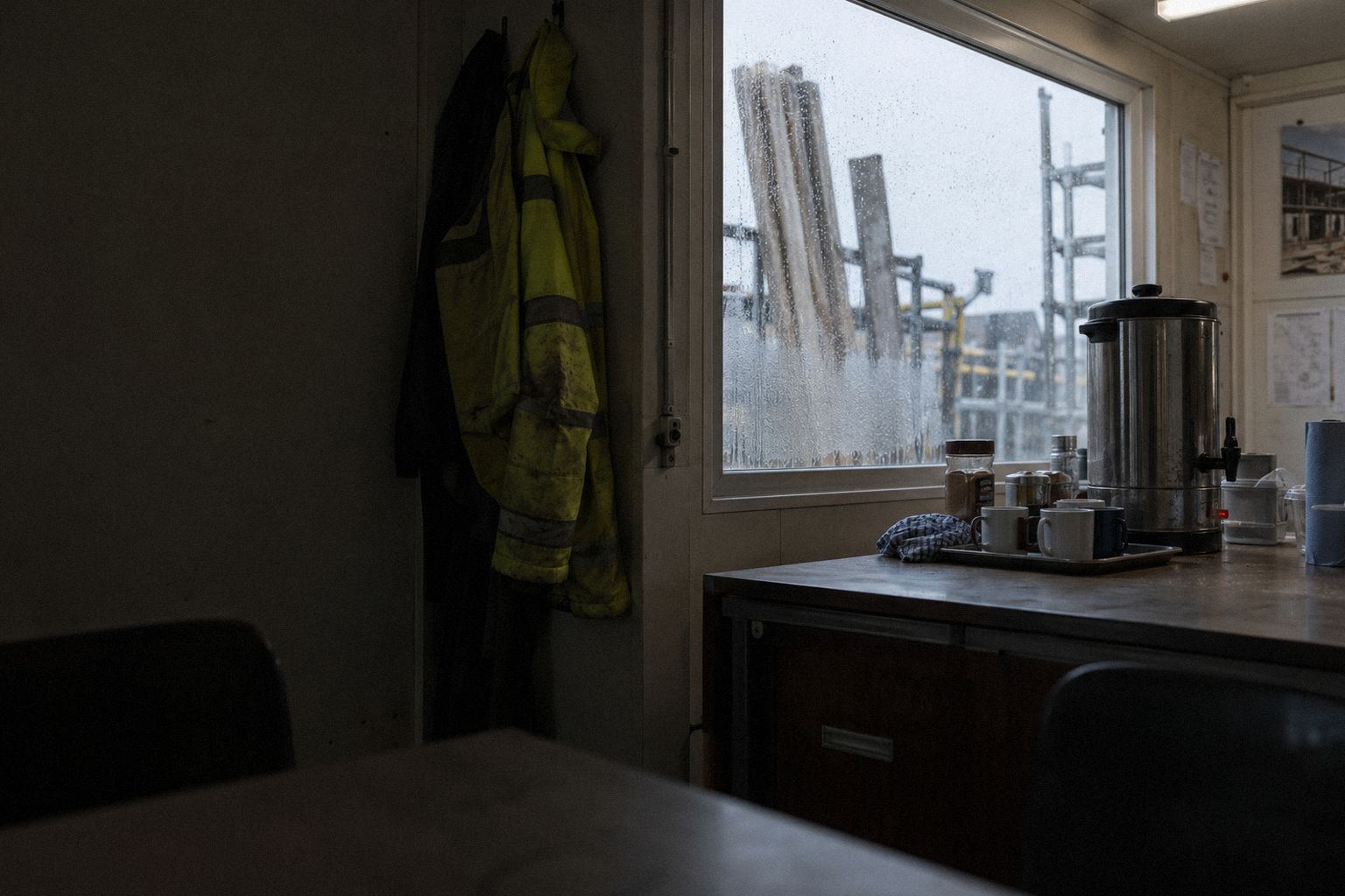 A site cabin at first light, a tea urn and scaffold boards outside the window.