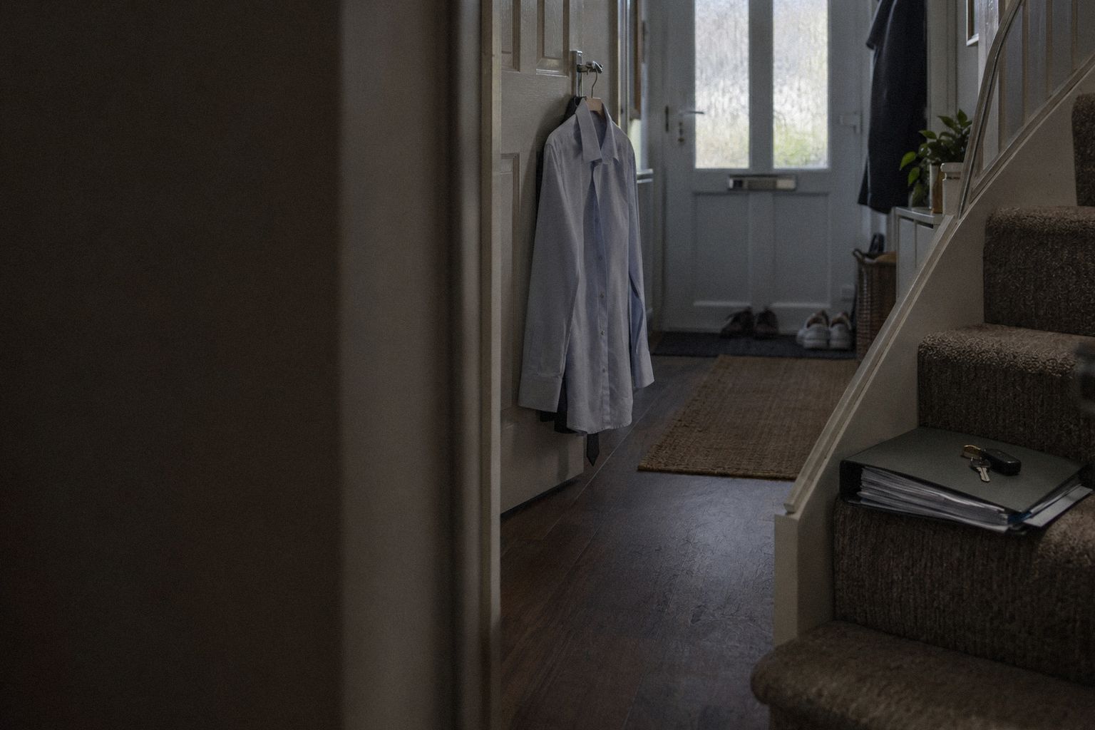A hallway at 7am, a pressed shirt on the door and a ring binder on the stair.