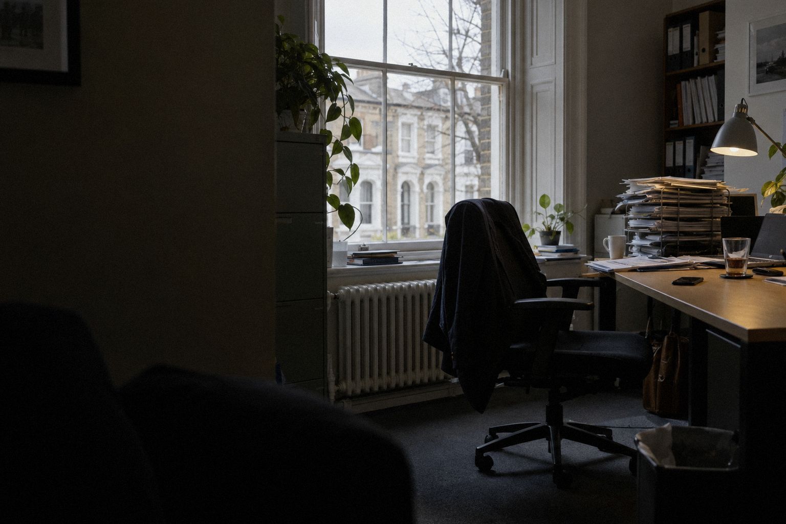 An office in an old building at 4pm, a phone face down beside a cold tea.