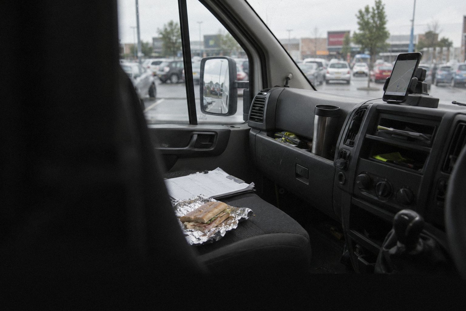 A van cab at lunchtime, a phone on the dashboard and a sandwich in foil.