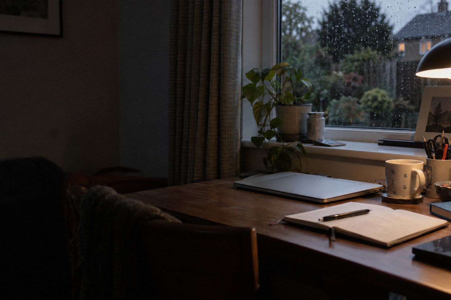 A tidy desk at dusk, a pen across a paper diary and the first rain on the window.
