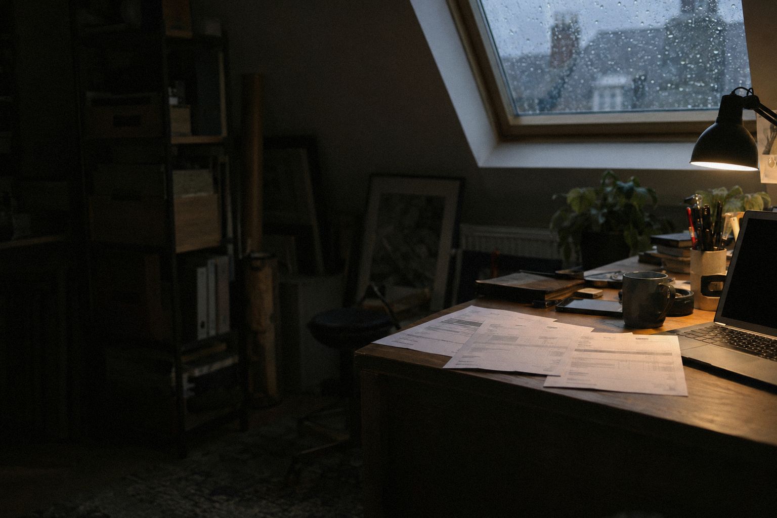 Three printed invoices fanned across a desk at 8pm, rain on the skylight.