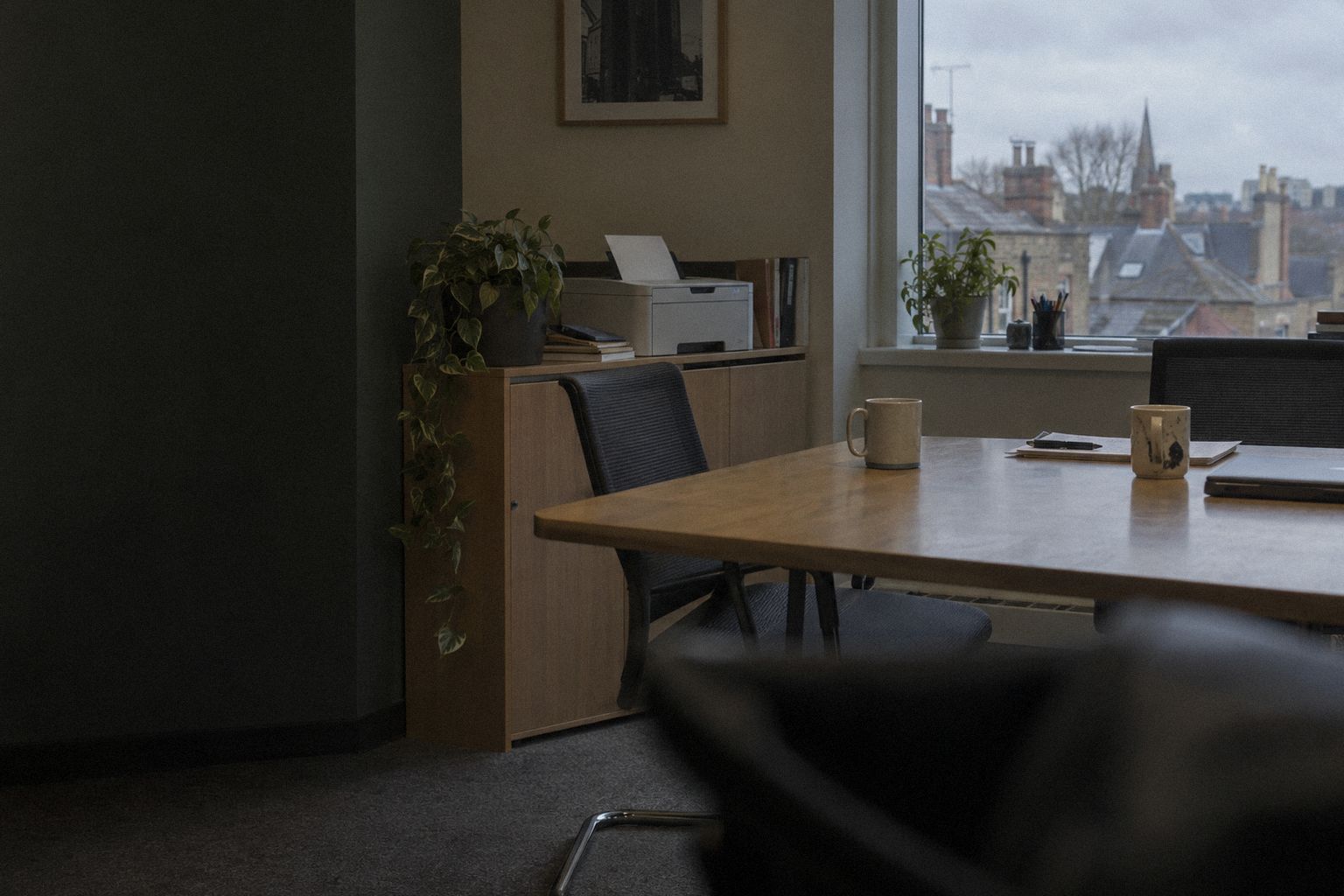 A meeting room at 5pm, two cold mugs and a printer finishing one page.