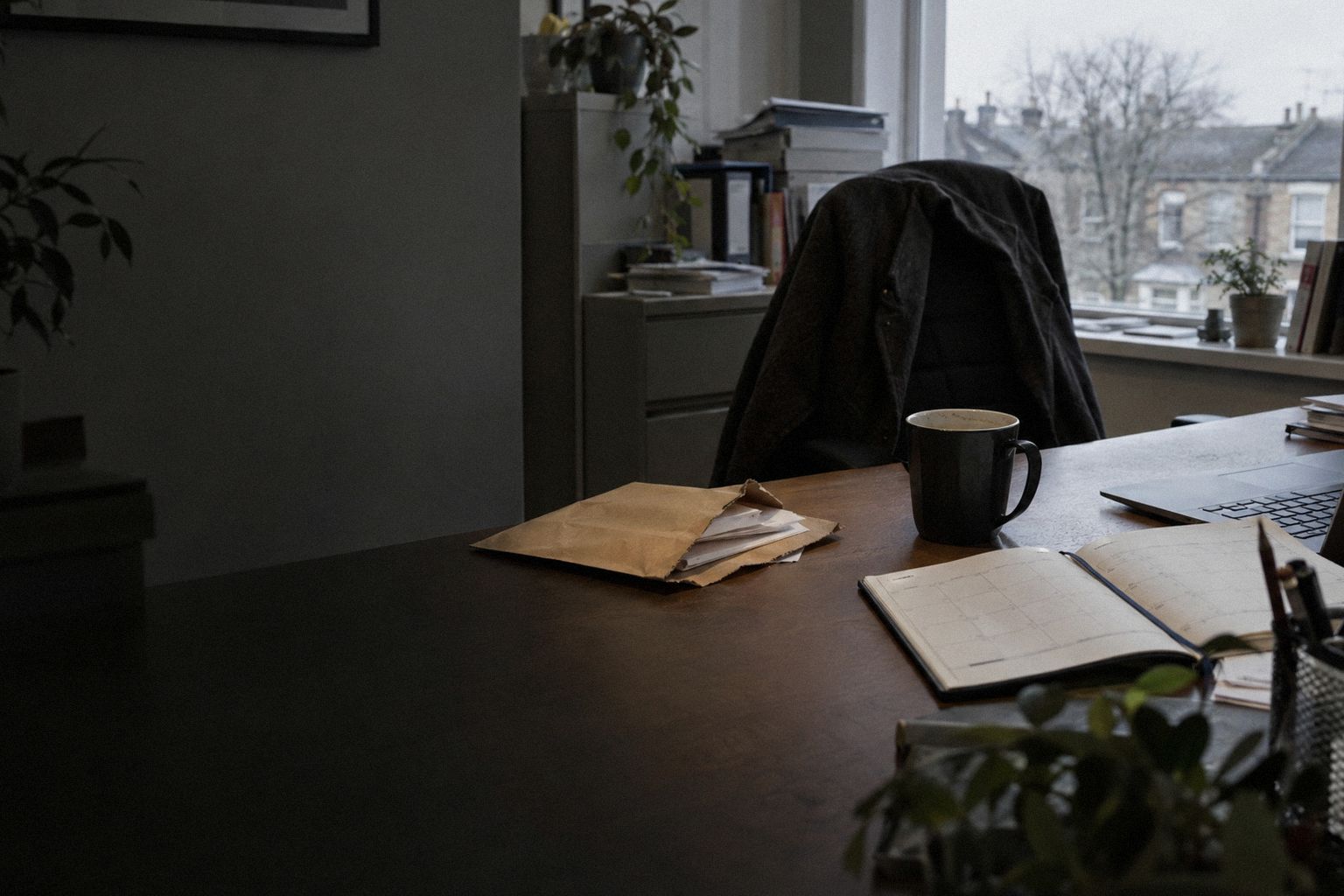 An office at 8am, a slit-open envelope beside a diary and a cold coffee.